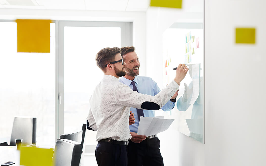 Employees discussing and writing on a glass board